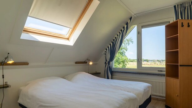 Ein Schlafzimmer mit Oberlicht, großem Fenster, einem Bett, Nachttischlampen und einem Holzschrank.