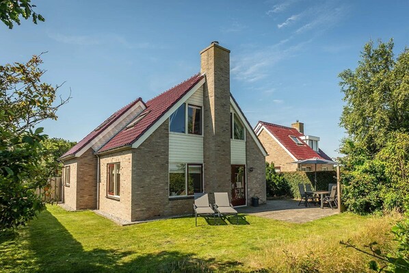 A modern two-story house with a sloped roof, a prominent chimney, and a well-maintained lawn. - Texel Getaway with Whirlpool (De Koog)