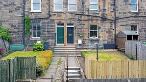 A terraced house with a front entrance, steps leading to the door, a small garden with a wooden fence, and a shed in the backyard. - Stylish 2-Bed Villa · Central Edinburgh (Edinburgh)