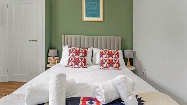 A bedroom with a bed, pillows, a bedside table, a lamp, a framed picture on the wall, and a door. - Stylish 2-Bed Villa · Central Edinburgh (Edinburgh)