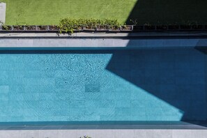 Ein Schwimmbecken mit klarem Wasser, umgeben von einer gefliesten Liegefläche und einer Rasenfläche mit Pflanzen.