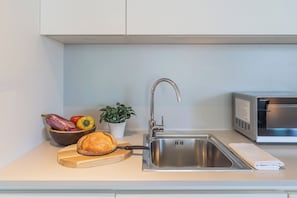 A kitchen with a stainless steel sink, a microwave, a bowl of vegetables, a loaf of bread, and a potted plant. - Laglio Élite Retreat - With Pool and Parking (Laglio)