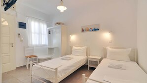 A hotel room with two single beds, a small desk, a chair, a wardrobe, and a window with curtains. - Kyanee (Adamantas)