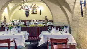 Un comedor interior con mesas dispuestas para dos, una araña y paredes de piedra.