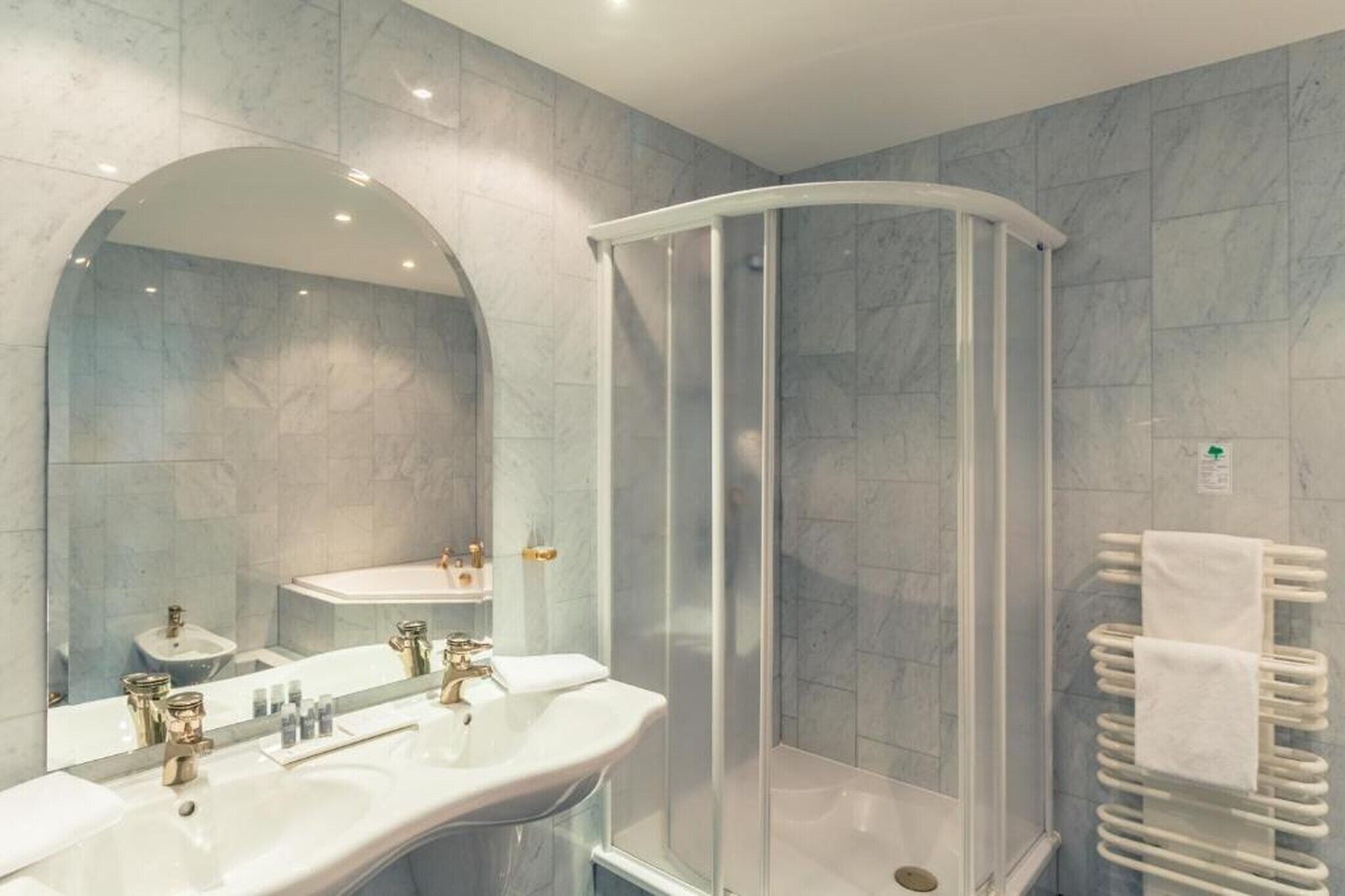 Ein modernes Badezimmer mit einer Duschkabine im Bogenstil, einem großen Spiegel und einem weißen Handtuchhalter.