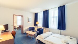 Habitación de hotel con cama, escritorio, silla, una mesita y ventana con cortinas.