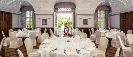 Uma sala de jantar formal com mesas redondas, cadeiras brancas e decoração elegante.