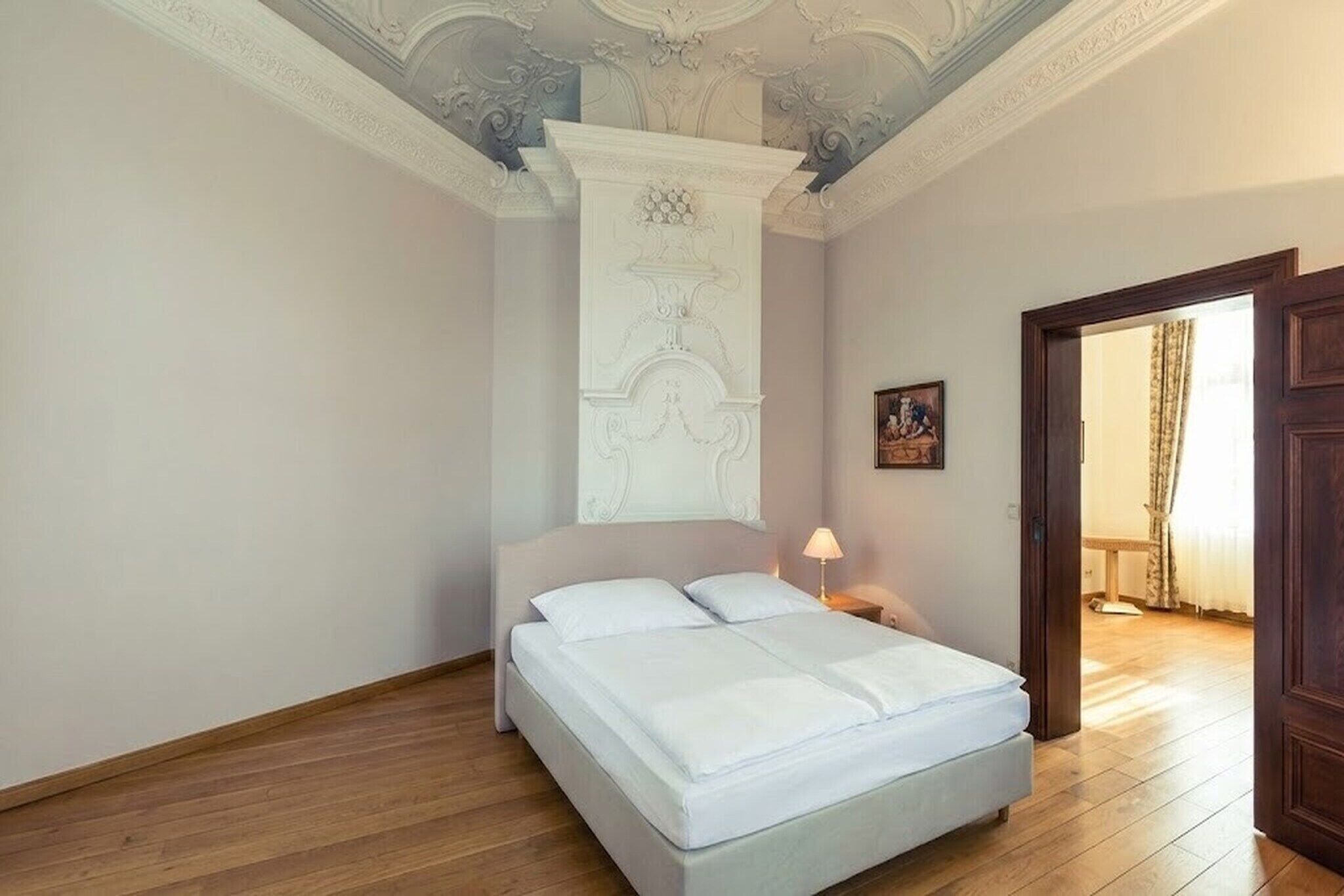 Een slaapkamer met een bed, nachtkastje, lamp en een deur naar een andere kamer.