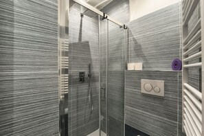 Een moderne badkamer met een glazen douchecabine, een handdoekhouder en een bedieningspaneel.