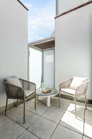 A balcony with two wicker chairs, a small round table, and a glass door leading to a covered area. - Charming penthouse in a prime location (Madrid)