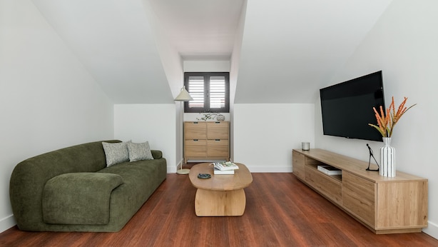 A modern living room with a green sofa, a wooden coffee table, a TV, and a wooden cabinet. - Charming penthouse in a prime location (Madrid)