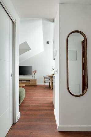 A modern interior with a wooden floor, a large mirror, a television, and a small table with a vase. - Charming penthouse in a prime location (Madrid)