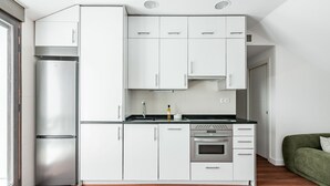 A modern kitchen with white cabinets, a stainless steel refrigerator, a built-in oven, and a green sofa in the adjacent living area. - Charming penthouse in a prime location (Madrid)