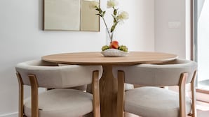 A round wooden dining table with four upholstered chairs, a vase with flowers, and a modern abstract painting on the wall. - Charming penthouse in a prime location (Madrid)
