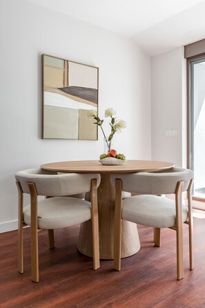 A round wooden dining table with four upholstered chairs, a vase with flowers, and a modern abstract painting on the wall. - Charming penthouse in a prime location (Madrid)