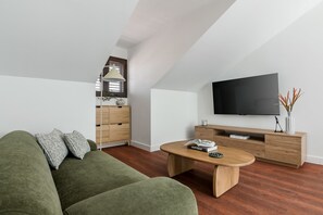 A modern living room with a green sofa, wooden coffee table, and a TV on the wall. - Charming penthouse in a prime location (Madrid)
