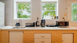 A modern kitchen with a sink, coffee maker, and microwave. There are two windows with a view of greenery outside. - Modern Studio Suite Near DC with Full Kitchen (Arlington)