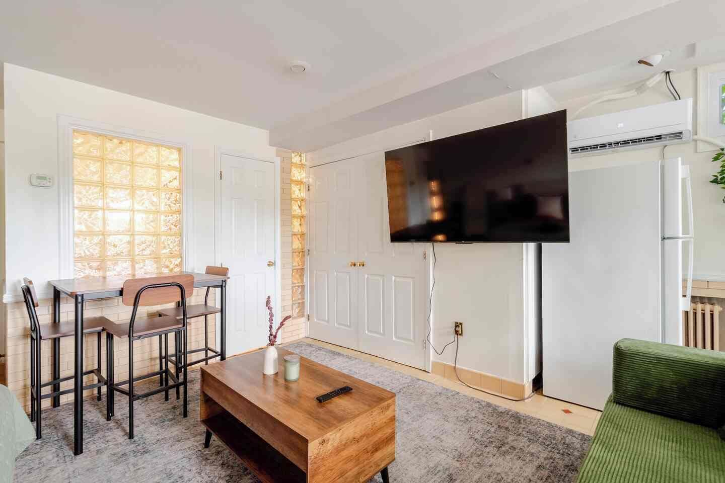 Un salon doté d’un téléviseur à écran plat fixé au mur, d’une table basse en bois, d’un canapé vert et d’un coin repas avec des chaises et une table.