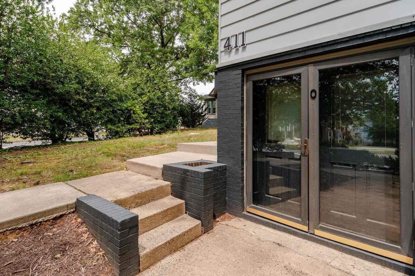 A modern building with a number 411 sign, a glass door entrance, and a concrete staircase leading to a patio area.