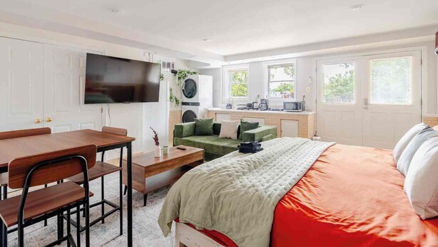 A modern bedroom with a bed, a desk, a green sofa, a TV, and a washing machine. - Modern Studio Suite Near DC with Full Kitchen (Arlington)