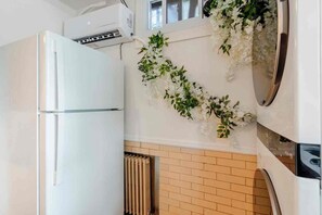 A kitchen with a white refrigerator, a wall-mounted air conditioner, and a radiator. - Modern Studio Suite Near DC with Full Kitchen (Arlington)