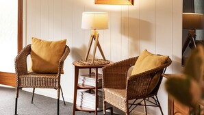 A room with two wicker chairs, a small round table with a lamp, and a mirror on the wall.