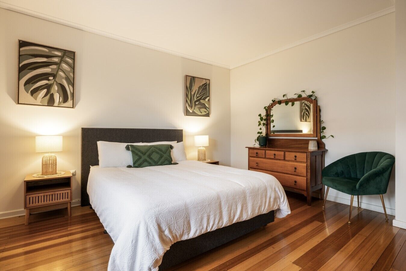 A bedroom with a bed, bedside tables, a dresser, a chair, and artwork on the walls.