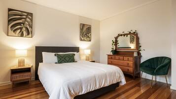 A bedroom with a bed, bedside tables, a dresser, a chair, and artwork on the walls.