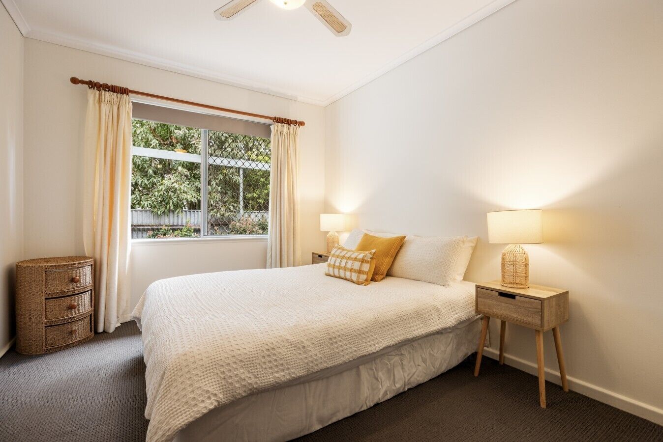 A bedroom with a bed, bedside lamps, a window with curtains, and a small wicker basket.