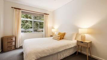 A bedroom with a bed, bedside lamps, a window with curtains, and a small wicker basket.