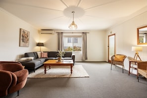 Una sala de estar con sofá, mesa de centro, una silla, lámpara y ventana con cortinas.