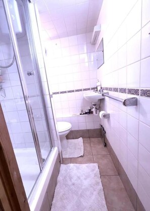 Ein Badezimmer mit Duschkabine, Toilette, Waschbecken und einem Handtuch auf dem Boden.