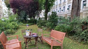 An outdoor seating area with two wooden chairs and a bench, a round table with a drink and a book, and a pair of shoes on the ground. - Property (London)