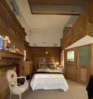 Ein Schlafzimmer mit Bett, Sessel, Kommode und Kamin.