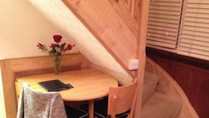 A small, cozy room with a wooden table and a single chair, a small sofa, and a vase with flowers. - Property (London)