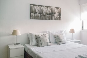 Ein ordentlich bezogenes Bett mit weißer Bettwäsche, zwei Nachttische mit Lampen und ein Wandbild mit Blumenmotiven.