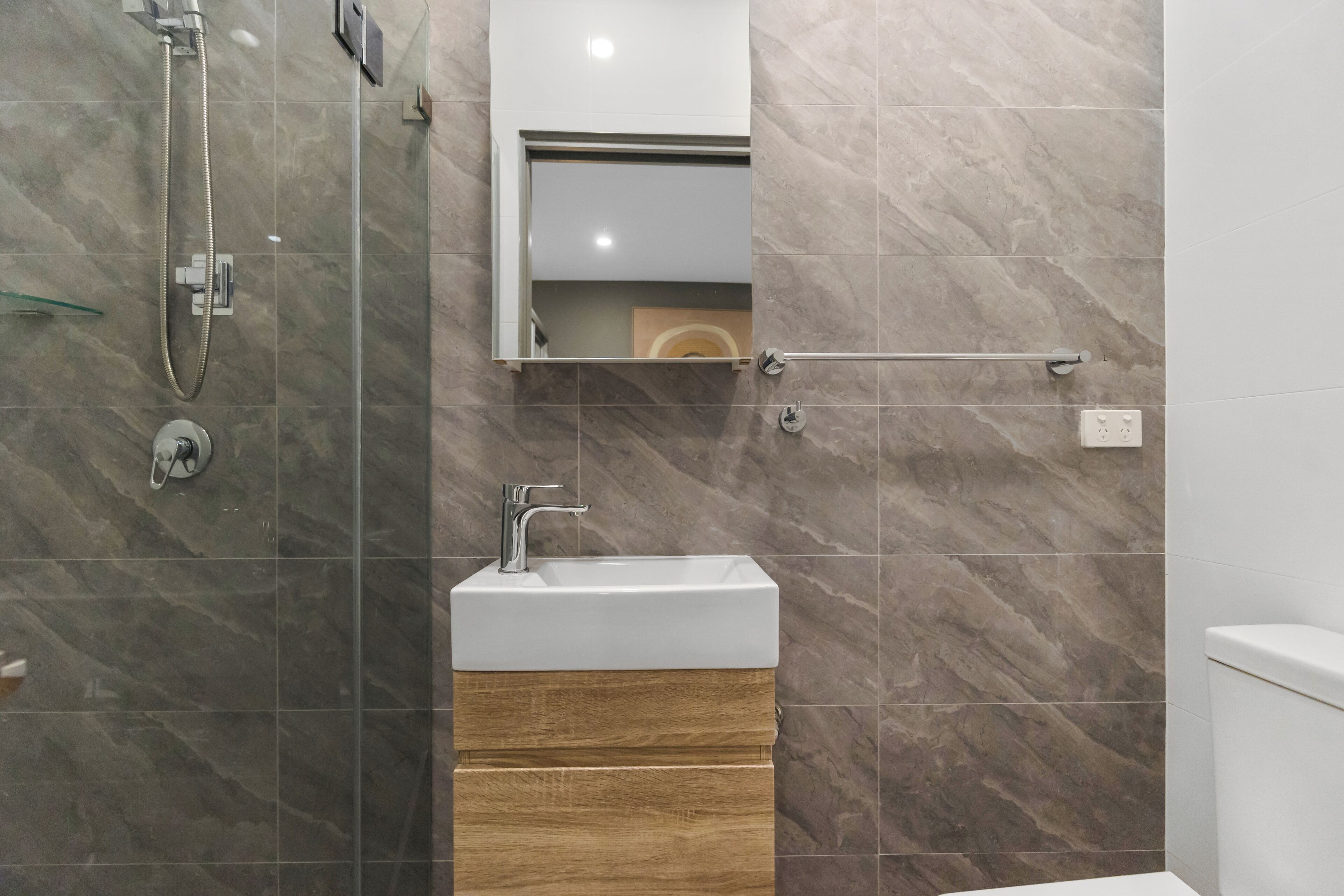A modern bathroom with a glass-enclosed shower, a white sink with a wooden vanity, and a mirror above the sink.