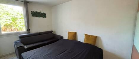 A bedroom with a bed, a sofa, and a window.