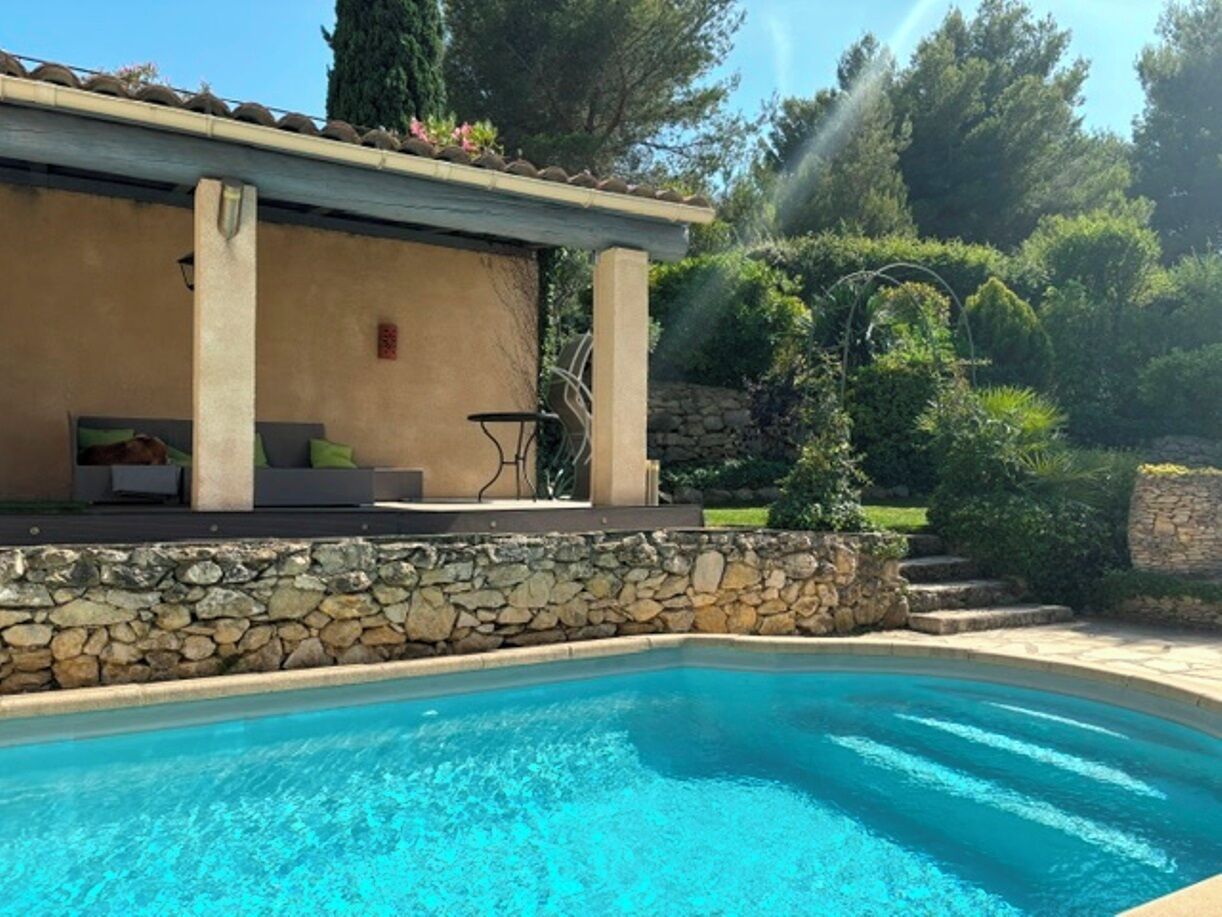 A swimming pool with a stone wall and a covered seating area with cushions.
