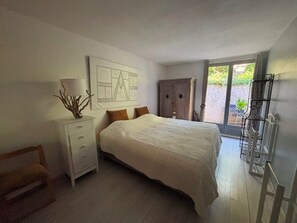 Ein Schlafzimmer mit Bett, Nachttisch, Kommode und einem Fenster mit Blick auf Grünflächen.