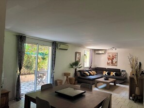 Ein Wohnzimmer mit einer Couch, einem Couchtisch und einem Esstisch. Ein großes Schiebeglastür führt zu einem Außenbereich.