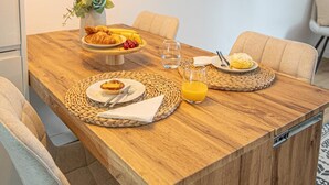 Zona pranzo con tavolo in legno, sottopiatti intrecciati, un vaso con fiori e una televisione appesa al muro.