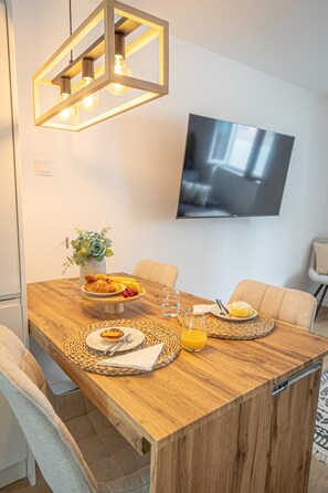 A dining area with a wooden table, woven placemats, a vase with flowers, and a television mounted on the wall. - MELISSA'S HOUSE
 2-bedroom house in pleasant Seixal with AC (Seixal)