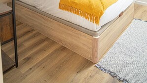 Una camera da letto con un letto, un pavimento in legno, una mensola in metallo nero e un condizionatore d'aria.