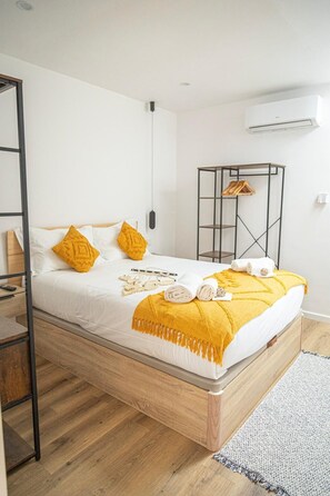 A bedroom with a bed, a wooden floor, a black metal shelf, and an air conditioning unit. - MELISSA'S HOUSE
 2-bedroom house in pleasant Seixal with AC (Seixal)