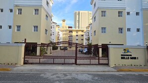 Um condomínio residencial com portão, vários edifícios, céu claro e uma placa indicando 'RESIDENCIAL BELLO MAR I'.