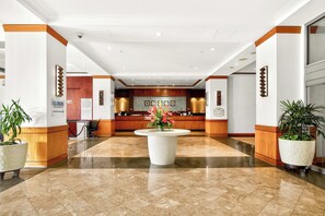 A hotel lobby with a reception desk, a large central planter with flowers, and potted plants. - Ilikai Luxury Suites | 1-Bd Ocean View | Free Parking and Car Incl. w/ 6 nights | ILK-937 by KBM (Honolulu)