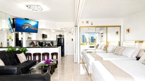 A modern hotel room with a large bed, a sofa, a dining area, and a view of the city. - Ilikai Hotel | 1-Bedroom Ocean View Suite | Car Incl. w/ 6 nights | ILK-937 by KBM (Honolulu)