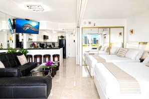 A modern hotel room with a large bed, a sofa, a dining area, and a view of the city. - Ilikai Hotel | 1-Bedroom Ocean View Suite | Car Incl. w/ 6 nights | ILK-937 by KBM (Honolulu)