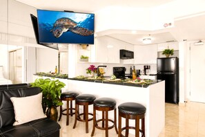A modern kitchen with a central island, bar stools, and a flat-screen TV mounted above the island. - Ilikai Luxury Suites | 1-Bd Ocean View | Free Parking and Car Incl. w/ 6 nights | ILK-937 by KBM (Honolulu)